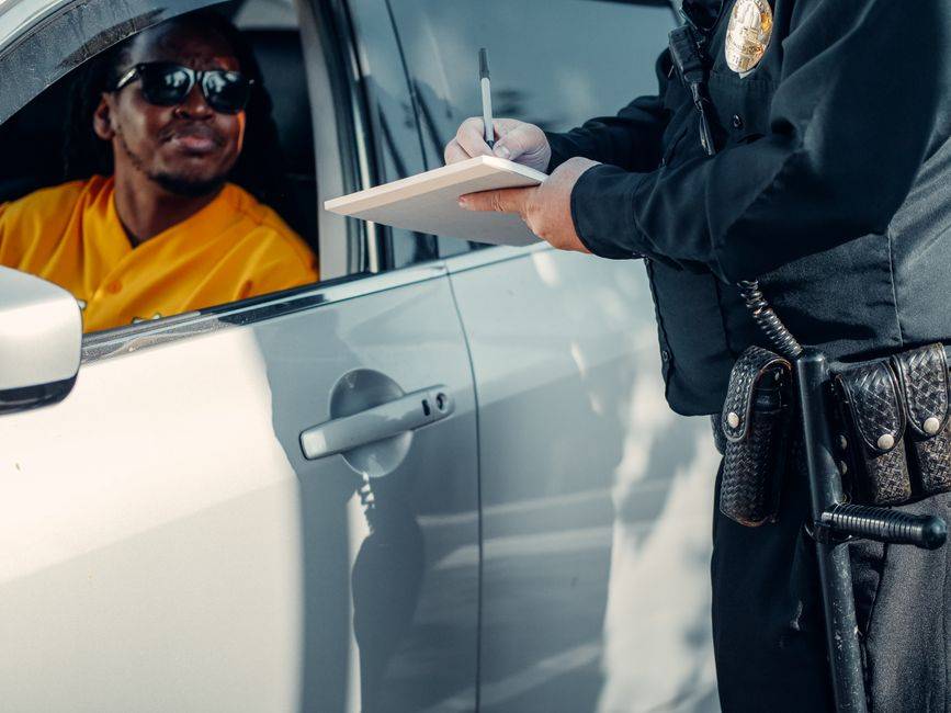 Radar routier : un conducteur arrêté après un ralentissement soudain A police officer writes a ticket for a driver in a car during a roadside stop.