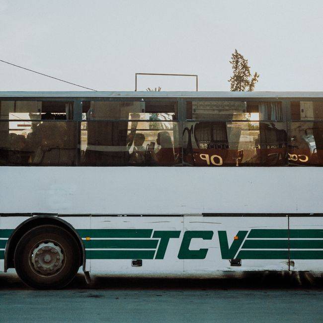 Side view of an urban public bus in cityscape during day with visible passengers.