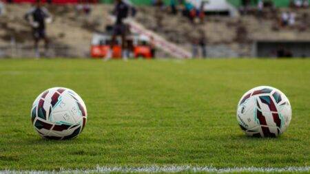CAN 2026 : battue par le Malawi, l’Algérie ira au Mondial 2027 Two soccer balls resting on a vibrant green football field before a match begins.