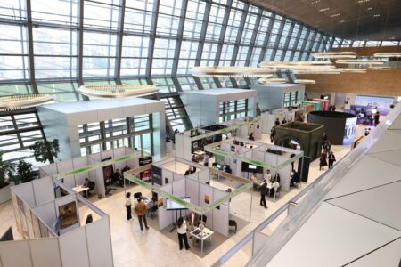 A bustling trade show exhibition inside a modern hall with people networking and exploring booths.