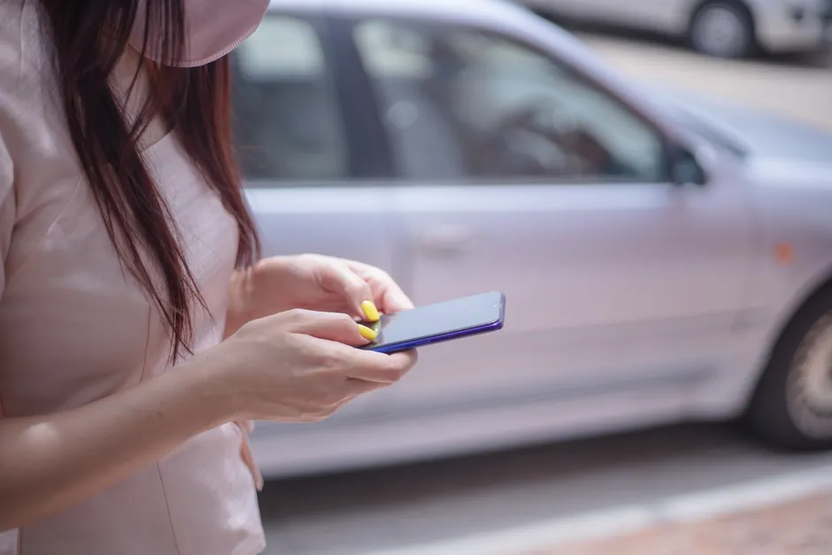 Paiement Wero face aux annonces en ligne : limites et précautions A close-up of a woman texting on a smartphone near a parked car outdoors.