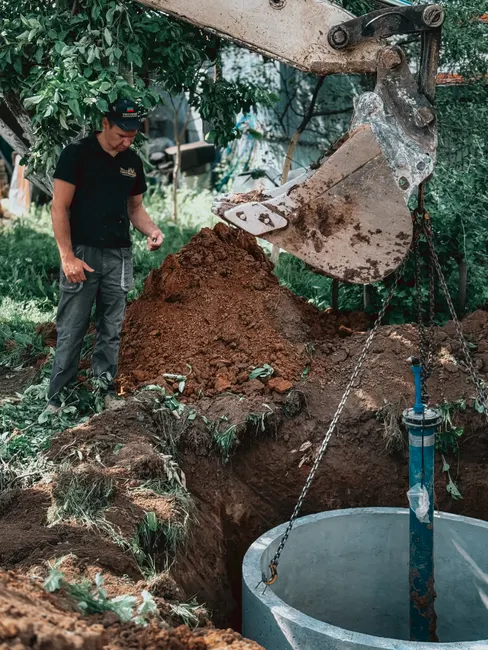 A construction worker supervises the installation of a concrete well using heavy machinery in a backyard project.