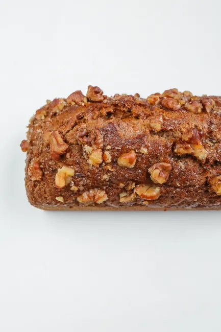 A delicious loaf of banana bread topped with walnuts against a clean, white background.