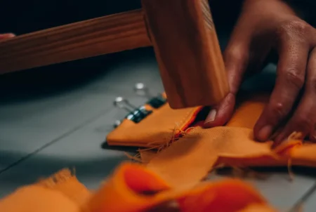 A detailed view of hands sewing fabric with a wooden hammer, emphasizing craftsmanship.