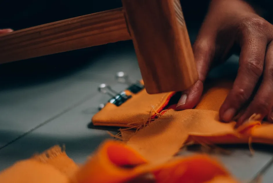 Pourquoi l’ONU utilise-t-elle un marteau islandais? A detailed view of hands sewing fabric with a wooden hammer, emphasizing craftsmanship.