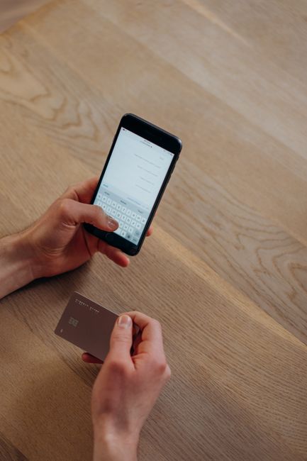 A person making a cashless transaction using a smartphone and credit card on a wooden table.
