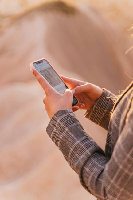 A person using a smartphone outdoors on a sunny day, checking messages.