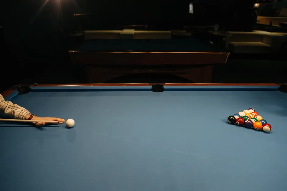 Dans l’Indre, quatre adresses pour jouer au billard A player's hand aiming at a cue ball on a billiard table with racked balls.