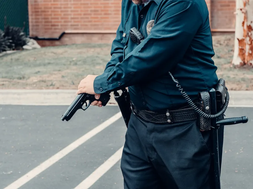 A police officer adjusting a firearm outdoors in a tactical situation, ensuring safety.