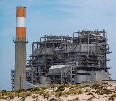 Sonelgaz au Bénin : réseaux électriques et gaz A power plant with smokestack on a sandy coastline, showcasing industrial architecture.
