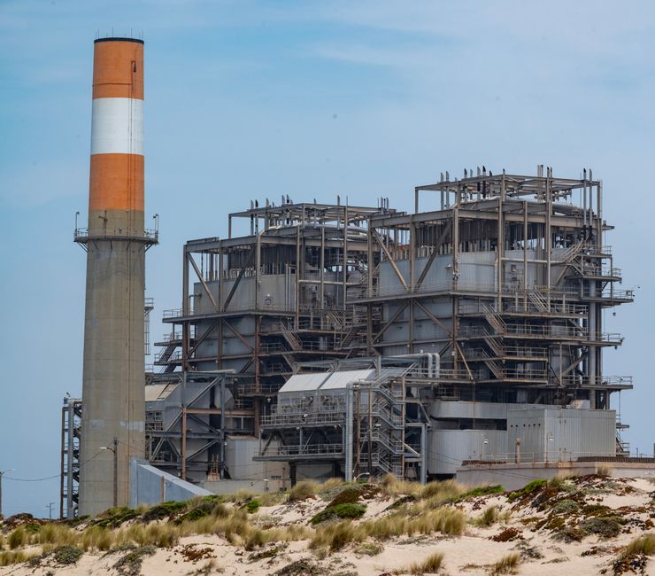 Sonelgaz au Bénin : réseaux électriques et gaz A power plant with smokestack on a sandy coastline, showcasing industrial architecture.