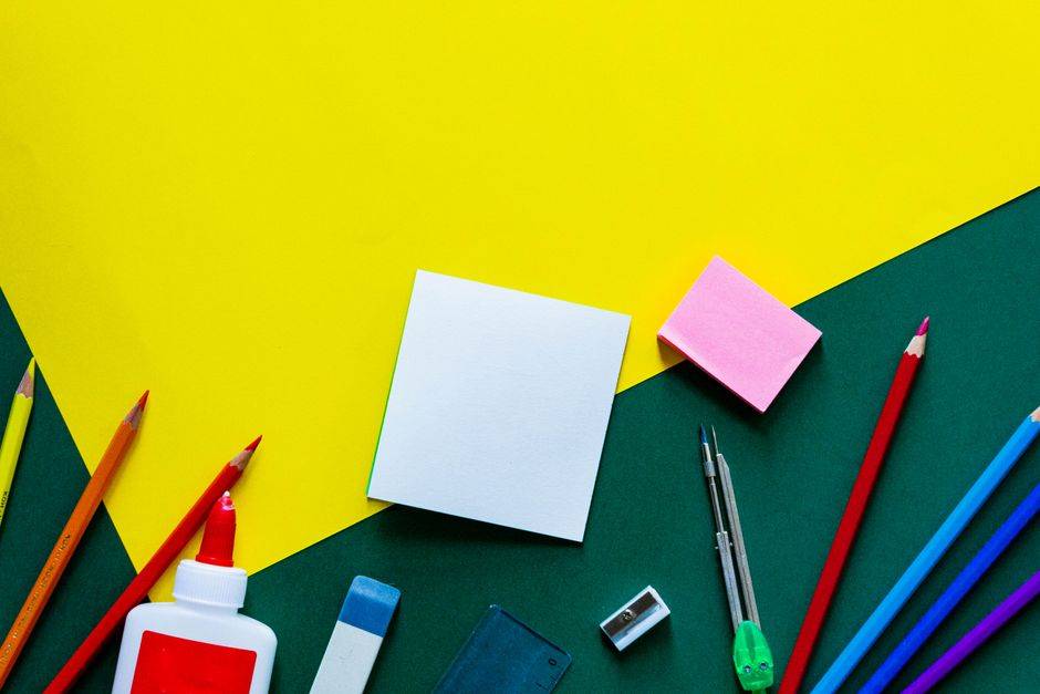 À Annaba, les fournitures scolaires locales s’exposent A vibrant flat lay of various school supplies on a yellow and green geometric background.