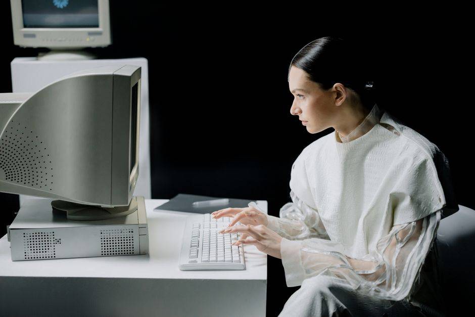 A woman in modern attire using a vintage computer in a dark setting, blending past and future.