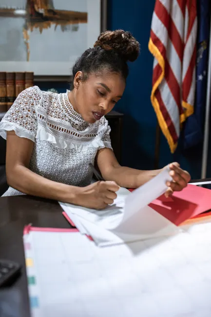 African American woman reviewing documents at an office desk, symbolizing leadership and dedication.
