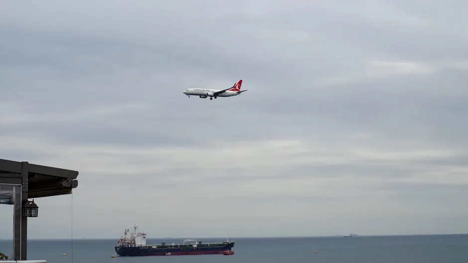 Une erreur d’IA militaire a failli provoquer une interception Airplane approaching over the sea with a cargo ship below under a cloudy sky.
