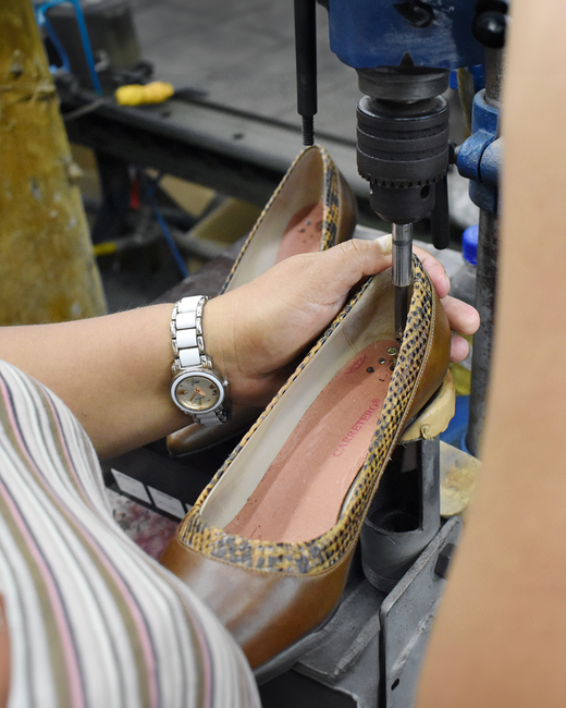 Artisan working with precision on a leather shoe in a factory setting.
