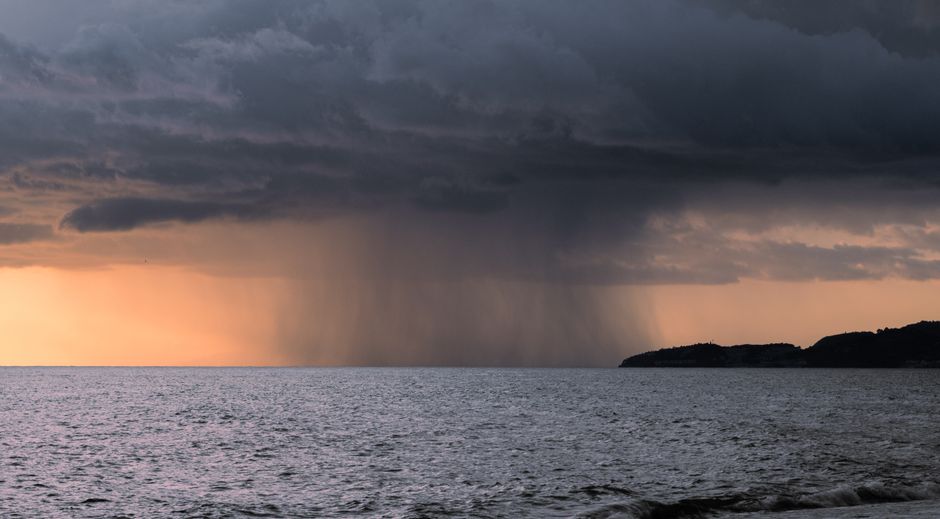 Captivating view of a rainstorm over the ocean at sunset, blending dark clouds and vibrant sky.
