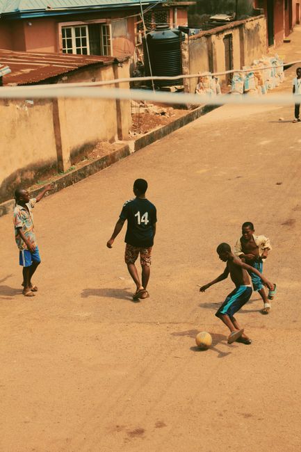 Children enjoying a lively game of football on a sunny street in Enugu, Nigeria.