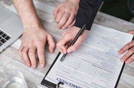 Assurance petite entreprise au Canada : les garanties à comparer Close-up image of two people signing an insurance policy document on a wooden desk.
