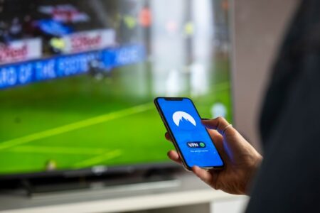 Paramount+ : catalogue, marques et accès en France Close-up of a person holding a smartphone with a VPN app, streaming sports on TV.