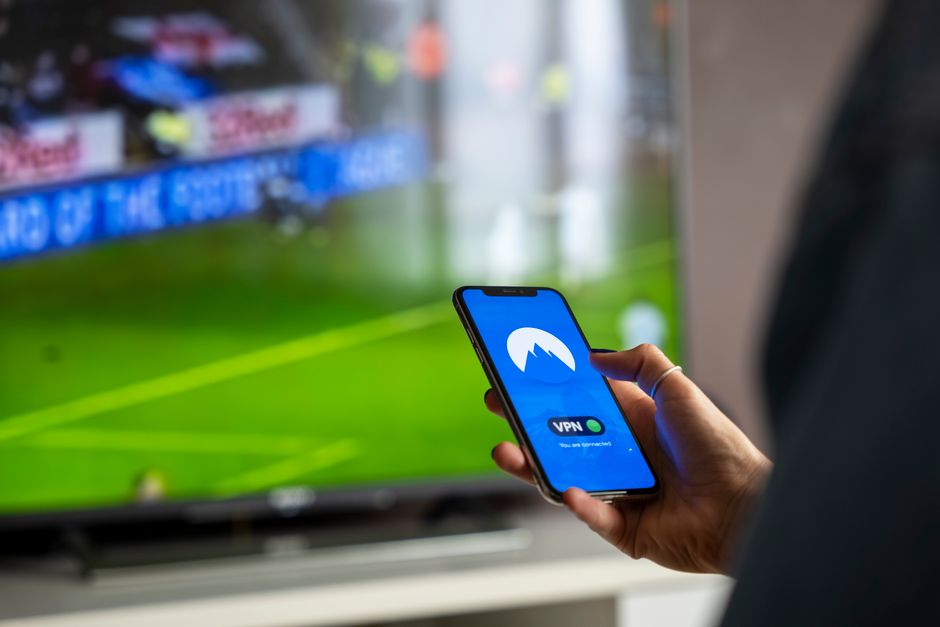 Paramount+ : catalogue, marques et accès en France Close-up of a person holding a smartphone with a VPN app, streaming sports on TV.