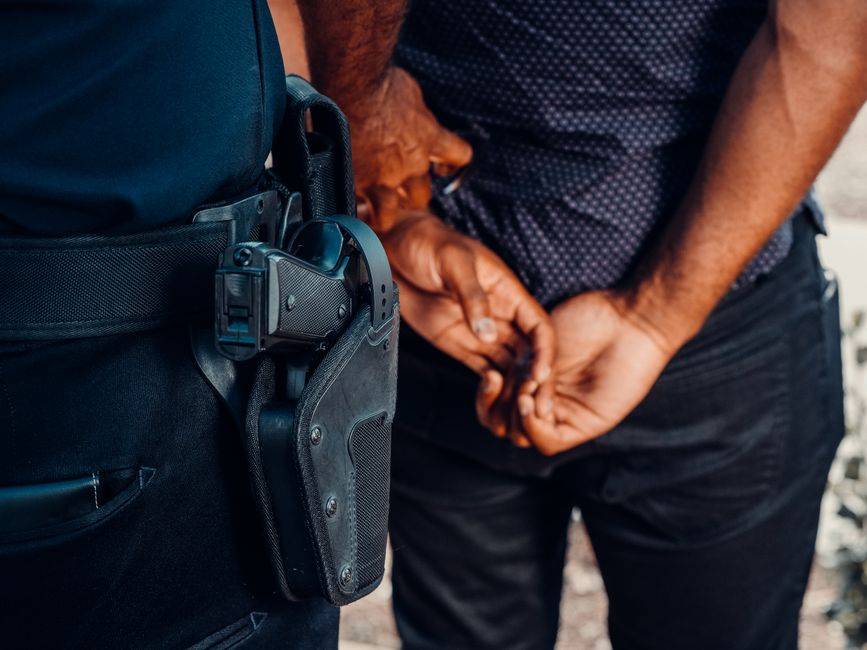 Espagne : 21 interpellations dans la « banque de la drogue » Close-up of a police officer arresting a suspect with visible firearm outdoors.