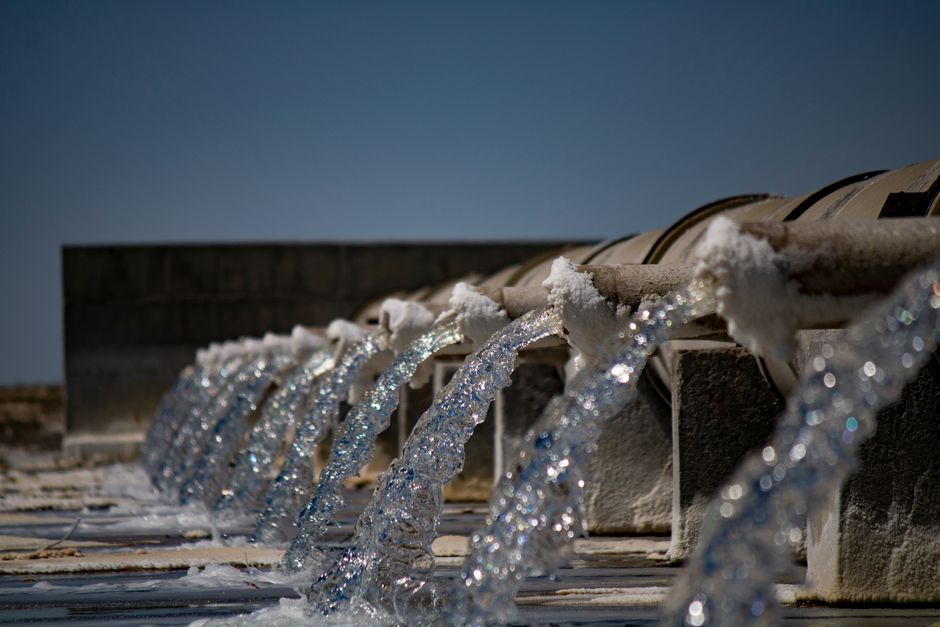 Close-up view of water flowing from industrial pipes against a clear blue sky.