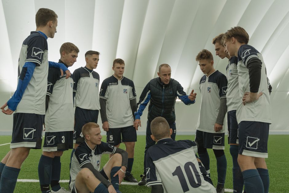 Coach giving a pep talk to a men's soccer team indoors.