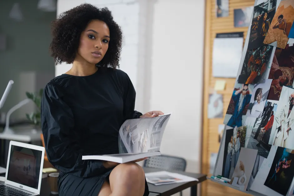 Blic Žena présente les femmes qui font le journal Elegant woman in a black dress holding a magazine in a modern office environment.