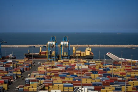 El Tarf : dix conteneurs algériens vers la Tunisie Expansive view of Orán's bustling port, showcasing colorful cargo containers and cranes by the sea.