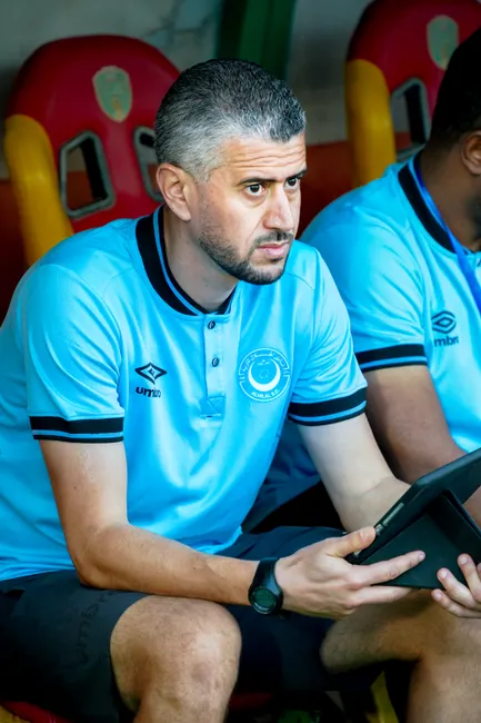 Football coach in blue jersey focused on analyzing game strategy using a tablet.