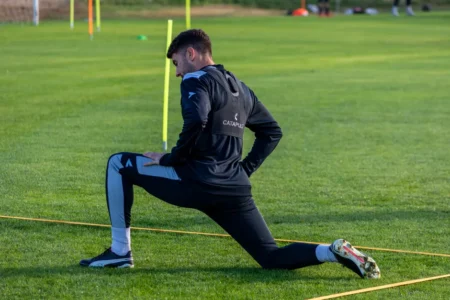 Les Verts accélèrent à Sidi Moussa avant la Zambie Football player stretching during outdoor training on a sunny day.