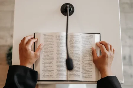 Hands holding an open Bible on a podium with a microphone. Ideal for religious or public speaking themes.