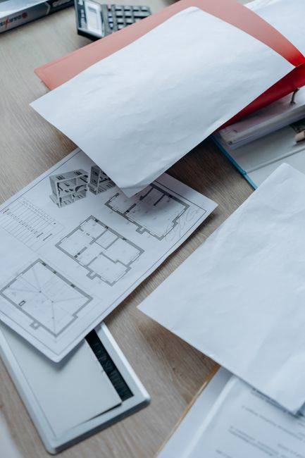 High angle view of architectural floor plans and paperwork on a wooden desk in an office setting.