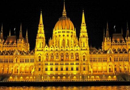 Illuminated Hungarian Parliament Building with reflection on Danube River at night.
