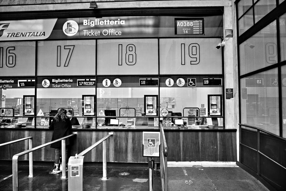 Algérie-Zambie : forte demande pour les billets à Tizi Ouzou Monochrome image of a train station ticket office with numbered counters, showcasing travel services.
