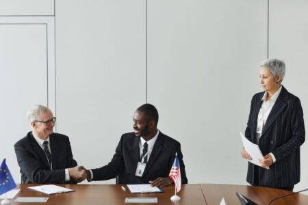 ONU : Ahmed Attaf représentera l’Algérie à New York en septembre 2026 Multinational business meeting with agreement signing, featuring diverse professionals and flags.