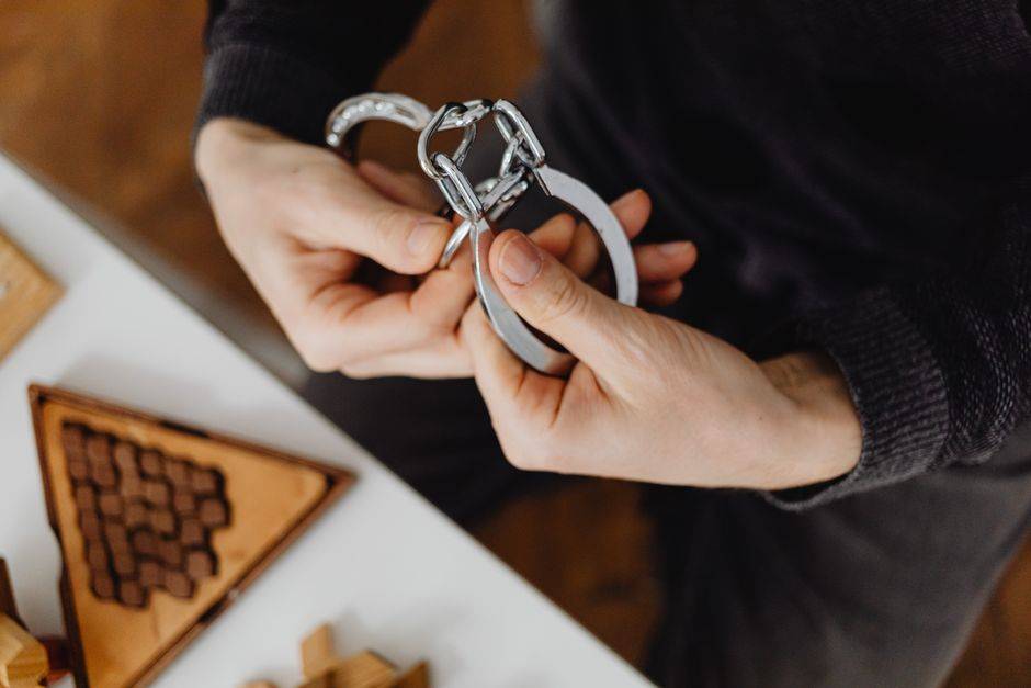 Person carefully handling silver handcuffs indoors, close-up view.