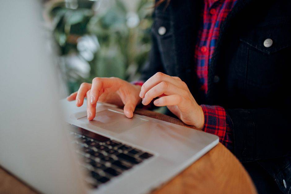 Hadj 2027 en Algérie : ouvrir son compte numérique Person wearing a plaid shirt typing on a laptop keyboard indoors, focusing on hands and device.