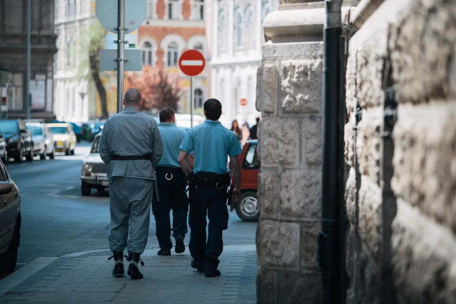 Policemen escort a handcuffed prisoner along a city street, showcasing law enforcement in action.