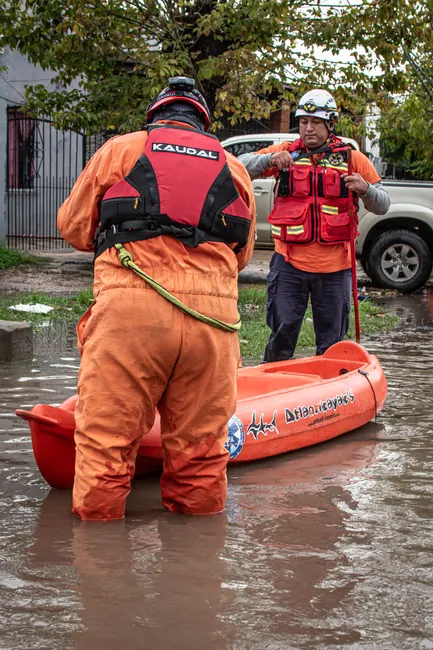 Rescue personnel in gear assist with flood relief, maneuvering a kayak through flooded streets.