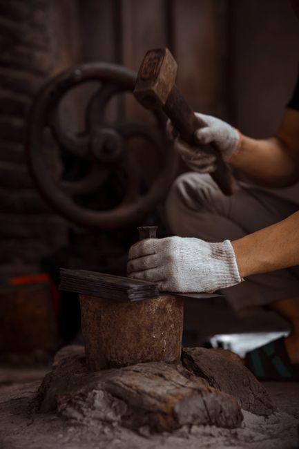 Skilled worker using a hammer to shape metal in a traditional workshop setting.