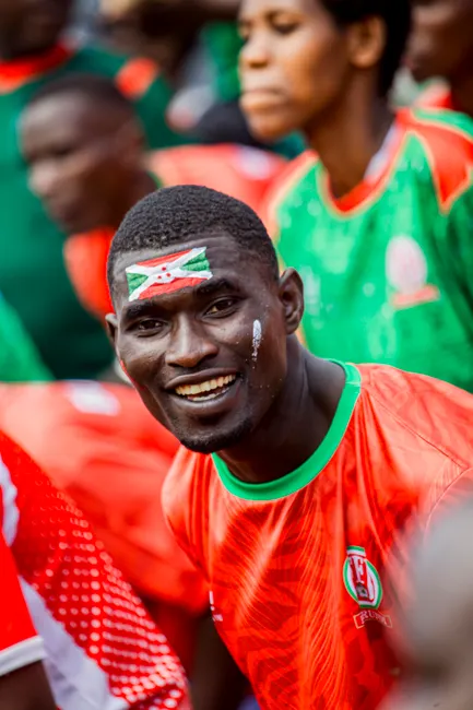 Smiling football fan with face paint and team jersey enjoying a match.