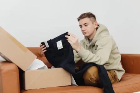Matelas compressé : quand dormir après le déballage? Teen sitting on sofa unboxing new clothes from a cardboard box.