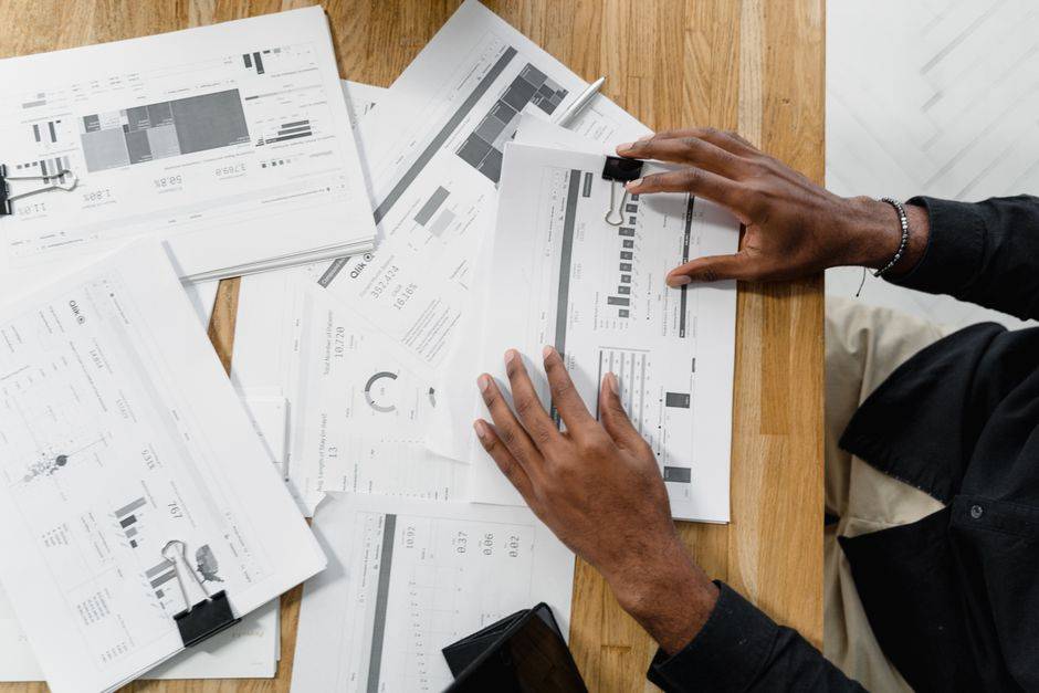 Top view of a professional reviewing financial documents at a wooden workspace.