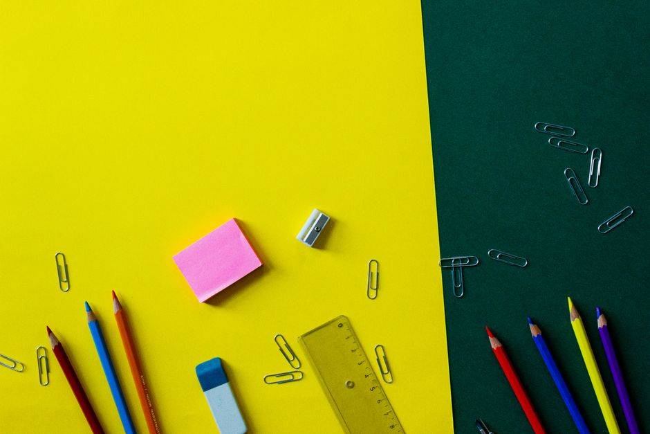 Top view of colorful school supplies on a vibrant yellow and green background.
