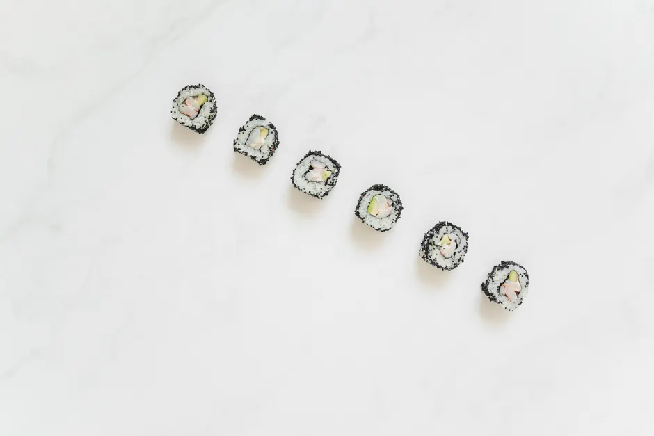 Top view of sushi rolls with sesame seeds on a marble counter. Minimalist style and aesthetic.