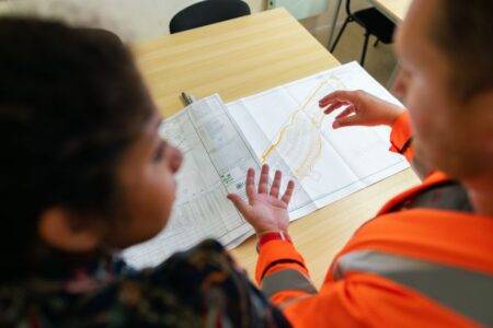 Ingénieur bureau d’études : missions, formation et salaire Two engineers reviewing construction blueprints on a table in an office setting.