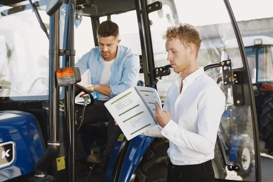 Two men reviewing documents near farm machinery, highlighting agricultural operation.