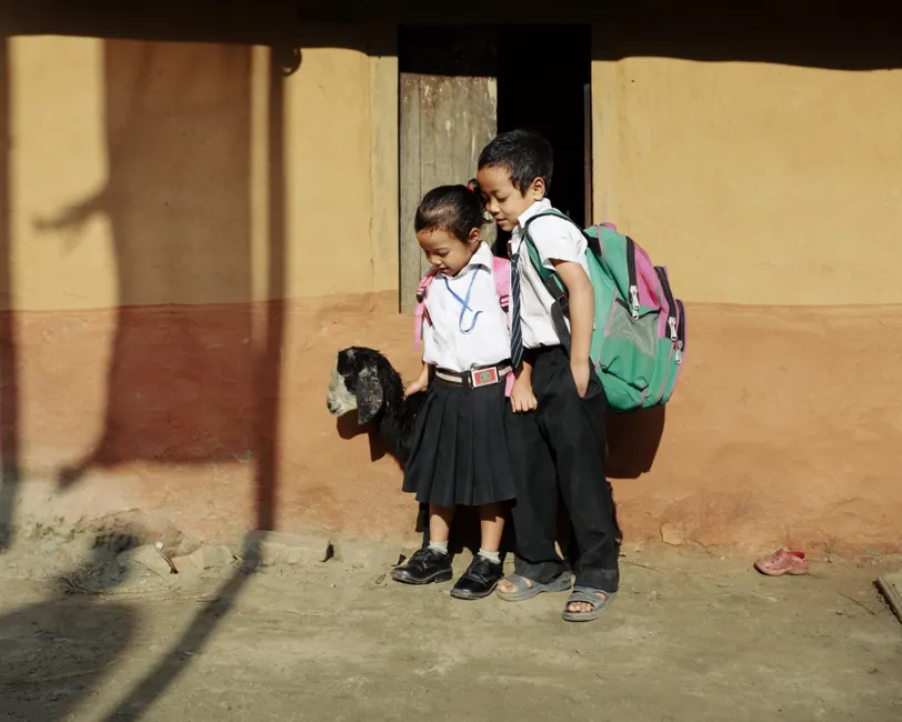 Rentrée scolaire en Algérie : trajet et accompagnement Two schoolchildren in uniforms holding a lamb outdoors, ready for school.